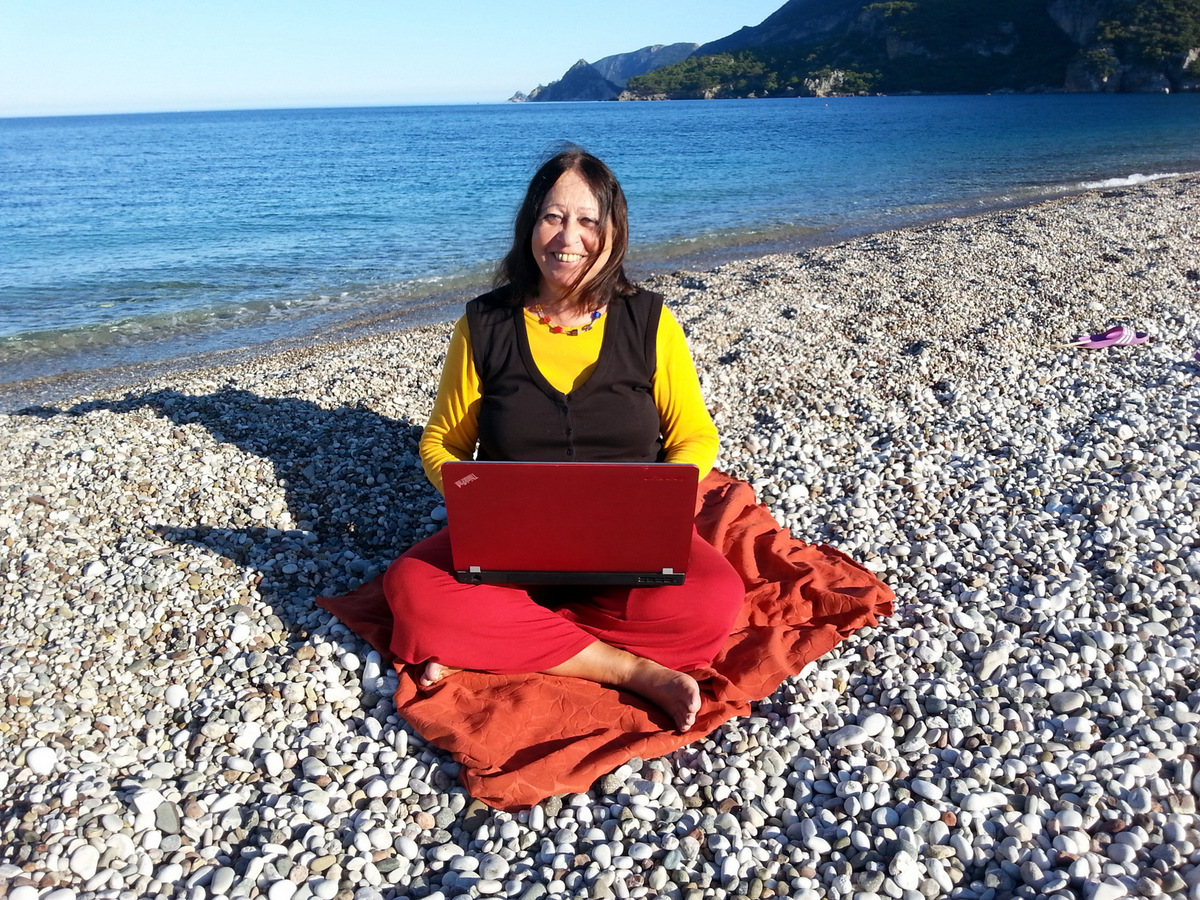 Mit Laptop am Meer Zamyat sitzt mit Laptop am Strand von Cirali auf einer roten Decke und lacht