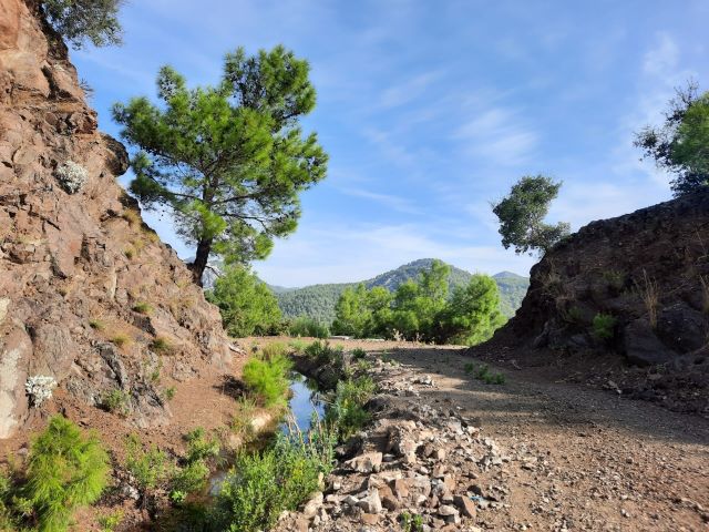 Kanalweg in der Türkei. Links ein kleiner Kanal neben einem Felsen, rechts daneben ein steiniger Weg