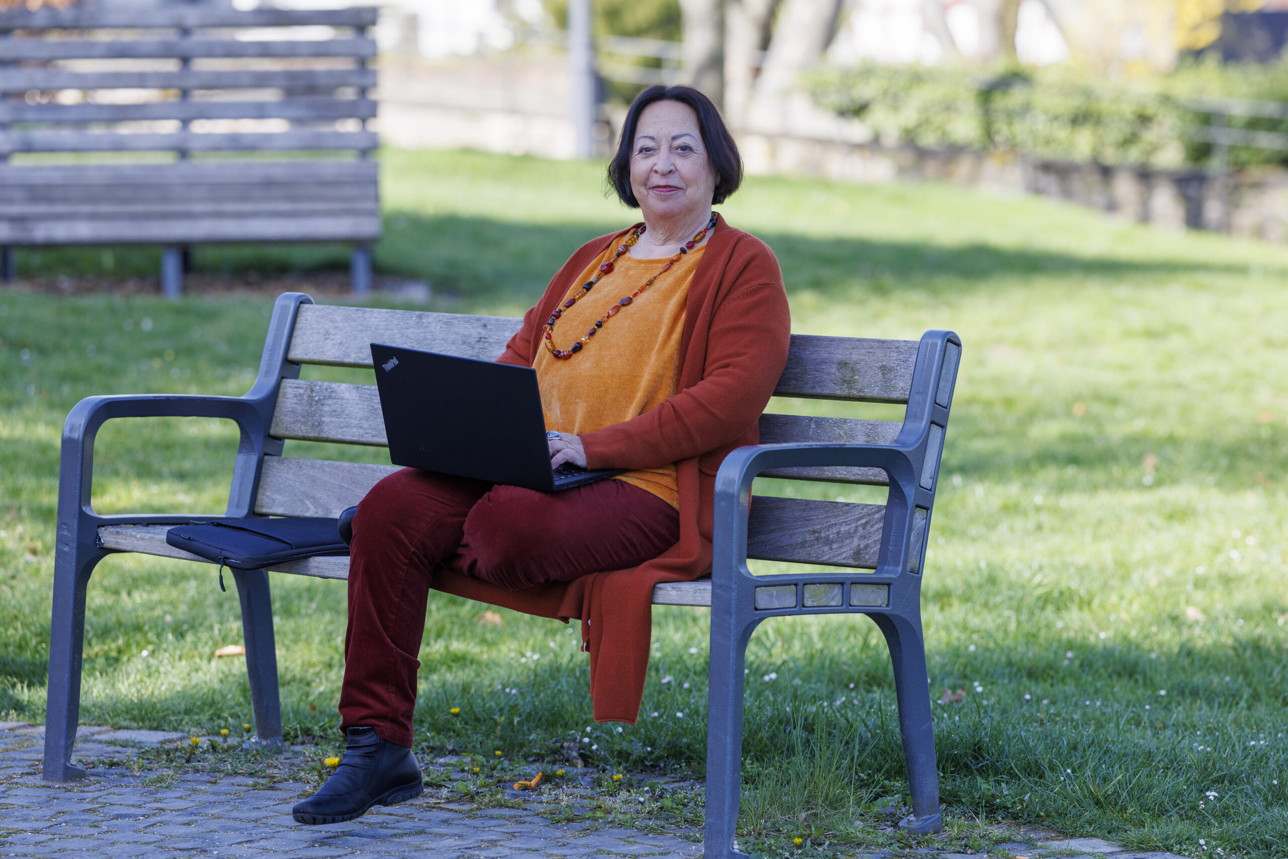 Zamyat mit Laptop auf einer Bank vor einer grünen Wiese.